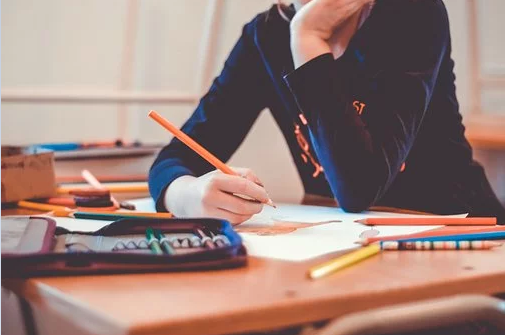 Ein Schulkind sitzt am Tisch und schreibt. Auf dem Tisch liegen viele bunte Stifte.