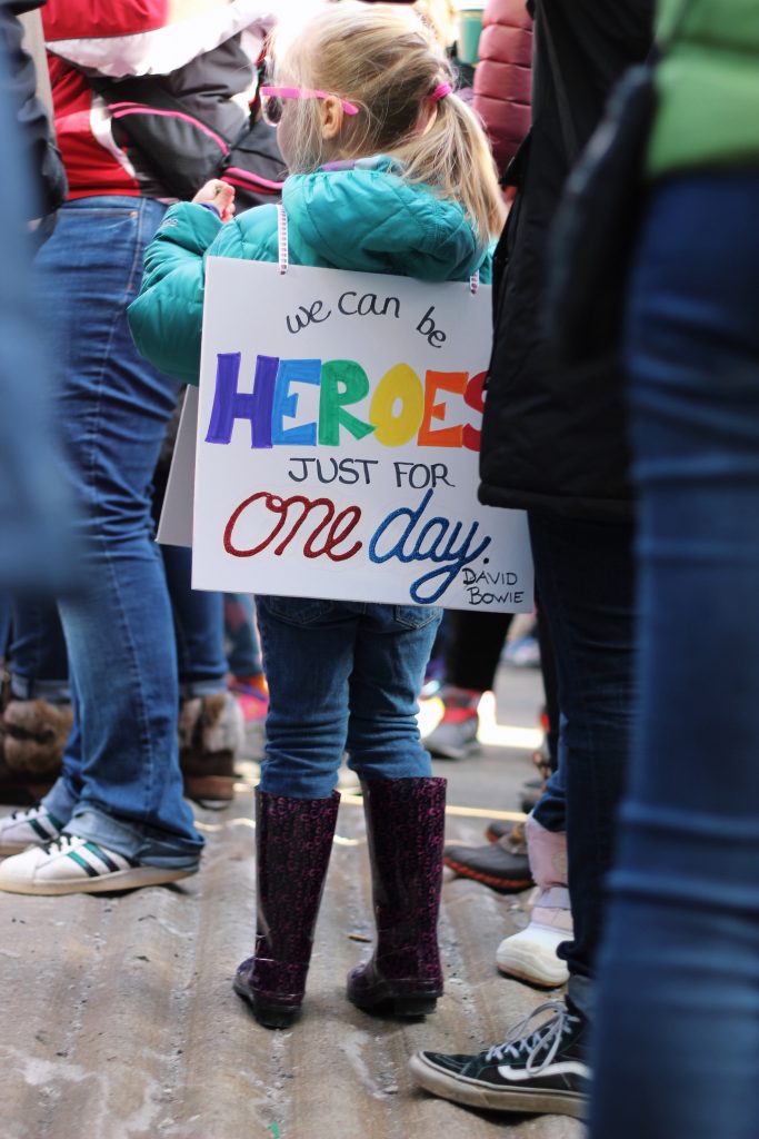 Ein Kind trägt ein buntes Schild auf dem steht, dass es ein*e Held*in sein kann