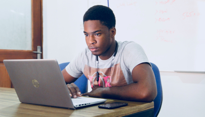 Ein Jugendlicher sitzt an einem Tisch vor einem Laptop.