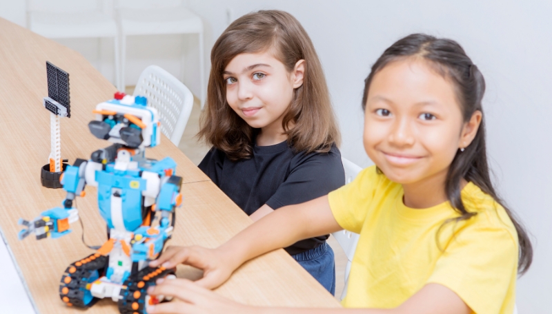 Zwei Mädchen lächeln in die Kamera und präsentieren ihren programmierten Roboter.